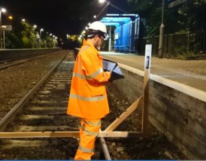 Surveyor on the rail track at night time checking a platform gauge for a tracck renewal rail survey